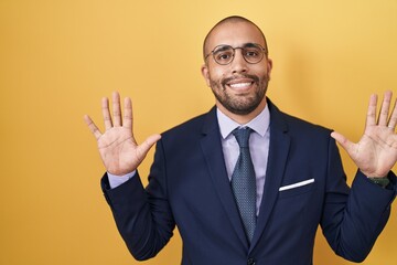 Hispanic man with beard wearing suit and tie showing and pointing up with fingers number ten while smiling confident and happy.