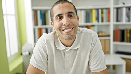 Young hispanic man student sitting smiling confident at library university