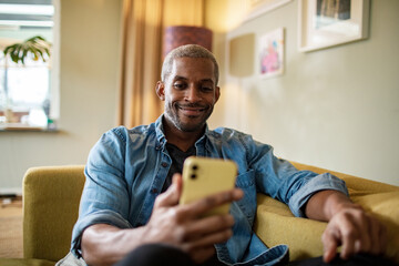 Middle aged man using a smartphone on the couch at home