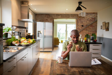 Middle aged African American male food blogger and nutritionist promoting a health supplement to his audience over a stream or video call on his laptop in the kitchen