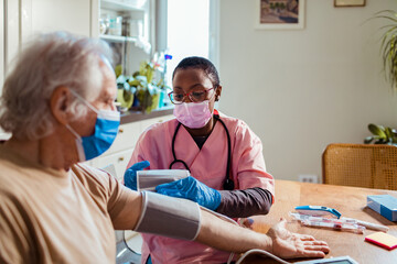 Young female caregiver measuring the blood pressure of her senior patient at their home