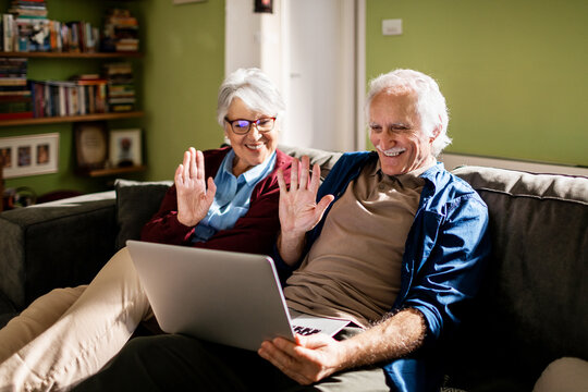 Senior couple waving to a person on a video call from the couch at home