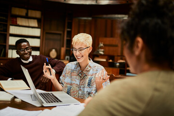 Young female student working on assignment with classmates in a college library