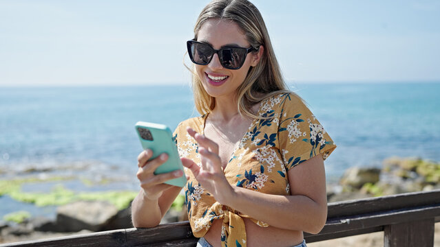 Young blonde woman tourist smiling confident using smartphone at seaside