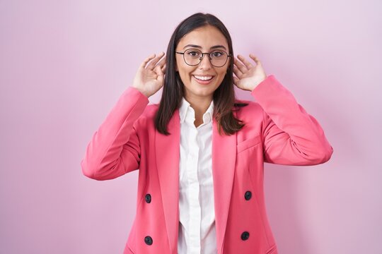 Young hispanic woman wearing business clothes and glasses smiling pulling ears with fingers, funny gesture. audition problem
