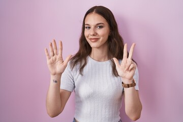 Young hispanic girl standing over pink background showing and pointing up with fingers number eight while smiling confident and happy.
