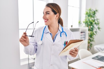 Young beautiful hispanic woman doctor smiling confident reading notebook at clinic