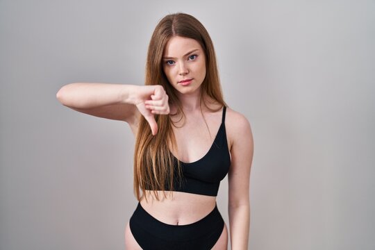 Young caucasian woman wearing lingerie looking unhappy and angry showing rejection and negative with thumbs down gesture. bad expression.