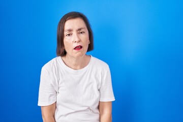 Middle age hispanic woman standing over blue background looking sleepy and tired, exhausted for...