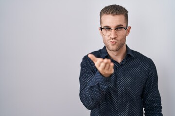 Young caucasian man standing over isolated background looking at the camera blowing a kiss with hand on air being lovely and sexy. love expression.