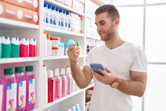Young caucasian man customer using smartphone holding deodorant at pharmacy