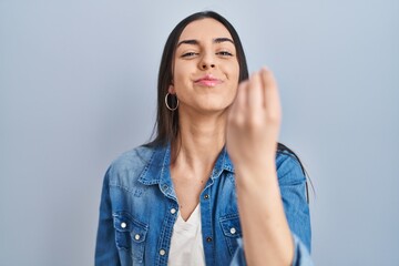 Hispanic woman standing over blue background doing italian gesture with hand and fingers confident expression - obrazy, fototapety, plakaty