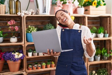 Young beautiful hispanic woman florist talking on smartphone using laptop at florist