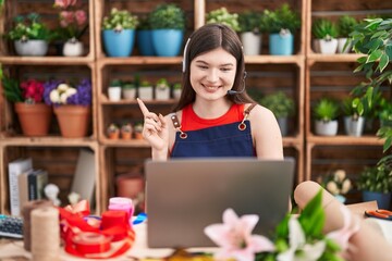 Young caucasian woman working at florist shop doing video call smiling happy pointing with hand and finger to the side