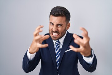 Handsome hispanic man wearing suit and tie shouting frustrated with rage, hands trying to strangle, yelling mad