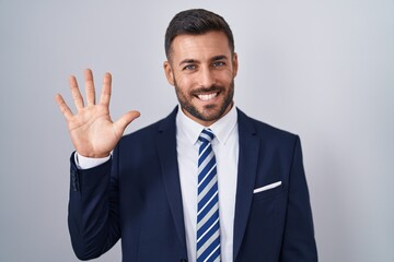 Handsome hispanic man wearing suit and tie showing and pointing up with fingers number five while...