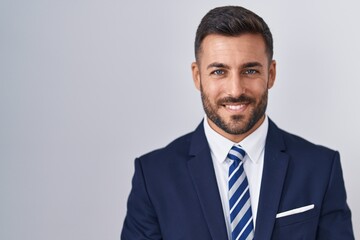 Handsome hispanic man wearing suit and tie with hands together and crossed fingers smiling relaxed and cheerful. success and optimistic