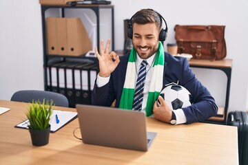 Handsome hispanic man watching football game at the office doing ok sign with fingers, smiling...