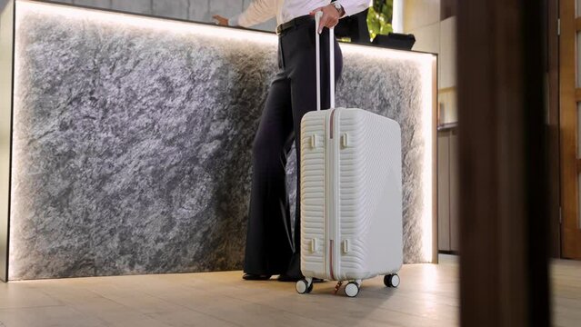 Business woman standing with her luggage by the hotel reception table