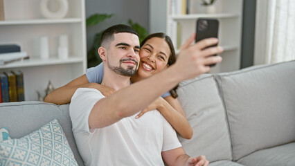 Obraz premium Beautiful couple making fun selfie memories on sofa, confidently smiling and expressing love at their cozy home