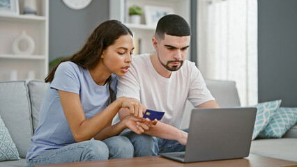 Beautiful couple in love, sitting together on sofa, engrossed in online shopping using a laptop and credit card, enjoying a relaxed lifestyle within their home's living room interior.