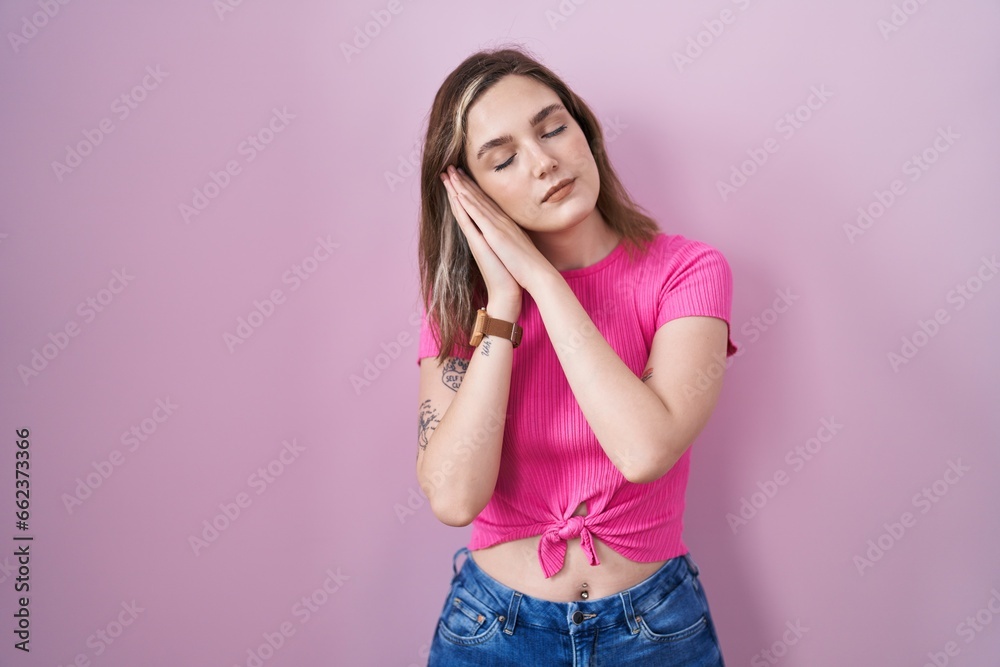 Sticker Blonde caucasian woman standing over pink background sleeping tired dreaming and posing with hands together while smiling with closed eyes.