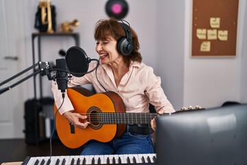 Middle age woman musician singing song playing electrical guitar at music studio