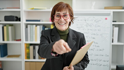 Mature hispanic woman teaching maths on magnetic board pointing with finger at library university