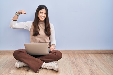 Young brunette woman working using computer laptop sitting on the floor strong person showing arm...