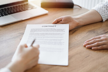 Business people signing contract papers while sitting at the wooden table in office, closeup. Partners or lawyers working together at meeting. Teamwork, partnership, success concept