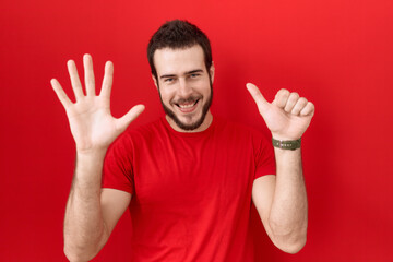 Young hispanic man wearing casual red t shirt showing and pointing up with fingers number six while smiling confident and happy.