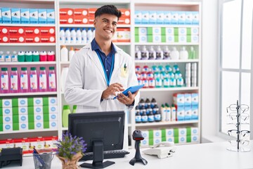 Young hispanic man pharmacist using touchpad working at pharmacy