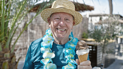 Senior grey-haired man tourist wearing summer hat and hawaiian lei holding ice cream at street