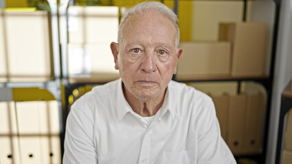 Senior grey-haired man ecommerce business worker sitting on table with relaxed expression at office