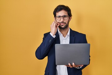 Handsome latin man working using computer laptop mouth and lips shut as zip with fingers. secret...