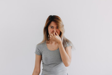 Unhappy Asian Thai woman wear grey, squeezing, pinching and holding nose blocking bad smell, smelly isolated on white background wall.