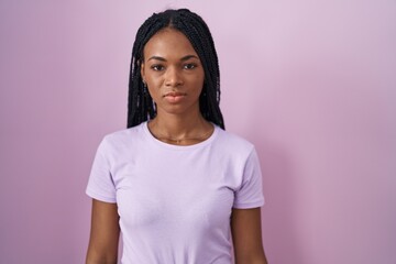 African american woman with braids standing over pink background relaxed with serious expression on face. simple and natural looking at the camera.