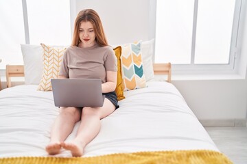 Young redhead woman using laptop sitting on bed at bedroom