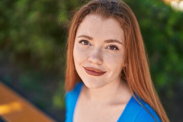 Young redhead woman smiling confident sitting on bench at park