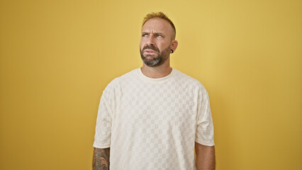 Attractive young man, a relaxed yet serious expression on his face, lost in his thoughts against an isolated yellow background, a doubt clouding his cool, casual lifestyle.