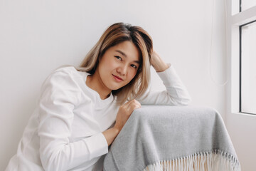 Asian Thai woman smiling face, thinking of good thing memories time, resting head on hand at apartment room in winter alone, looking at camera.