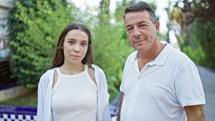 Obraz premium Confident father and his lovely daughter, two happy family members, standing together, enveloped in sunny park sunlight, joyfully smiling. their casual expression reflecting pure love and positivity.