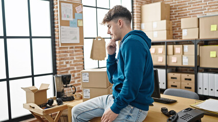Young hispanic man ecommerce business worker sitting on table thinking at office