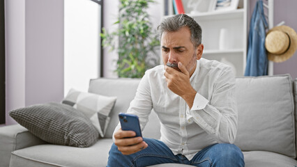 Upset young hispanic man, sporting grey hair and a beard, engrossed in a serious smartphone ordeal...