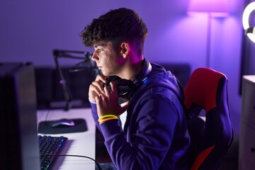Young hispanic teenager streamer holding headphones with relaxed expression at gaming room
