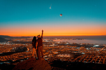 silhouettes of a couple standing on the top of the hill looking at starry night with Moon and...