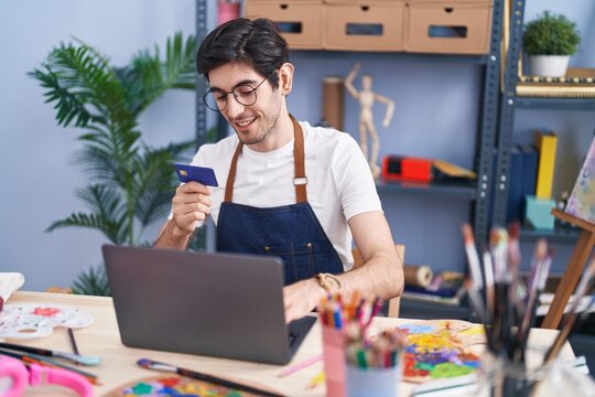Young hispanic man artist using laptop and credit card at art studio
