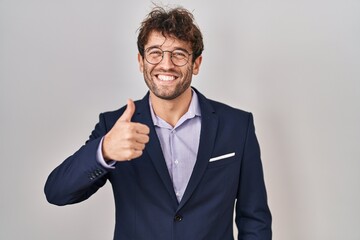 Hispanic business man wearing glasses doing happy thumbs up gesture with hand. approving expression looking at the camera showing success.