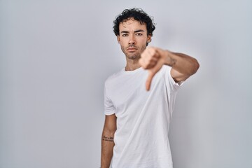 Hispanic man standing over isolated background looking unhappy and angry showing rejection and negative with thumbs down gesture. bad expression.