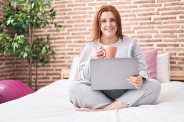 Young beautiful plus size woman using laptop drinking coffee at bedroom